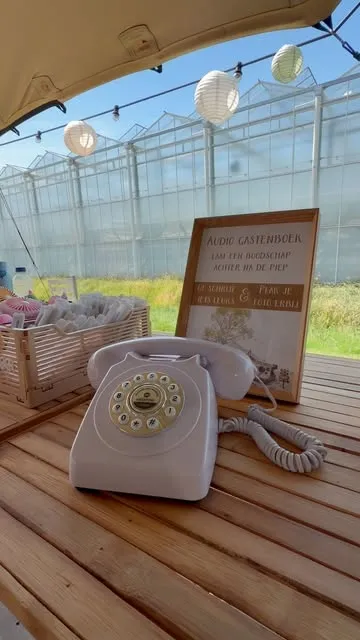 Een witte retrotelefoon op een houten tafel in een kas met lichtsnoeren