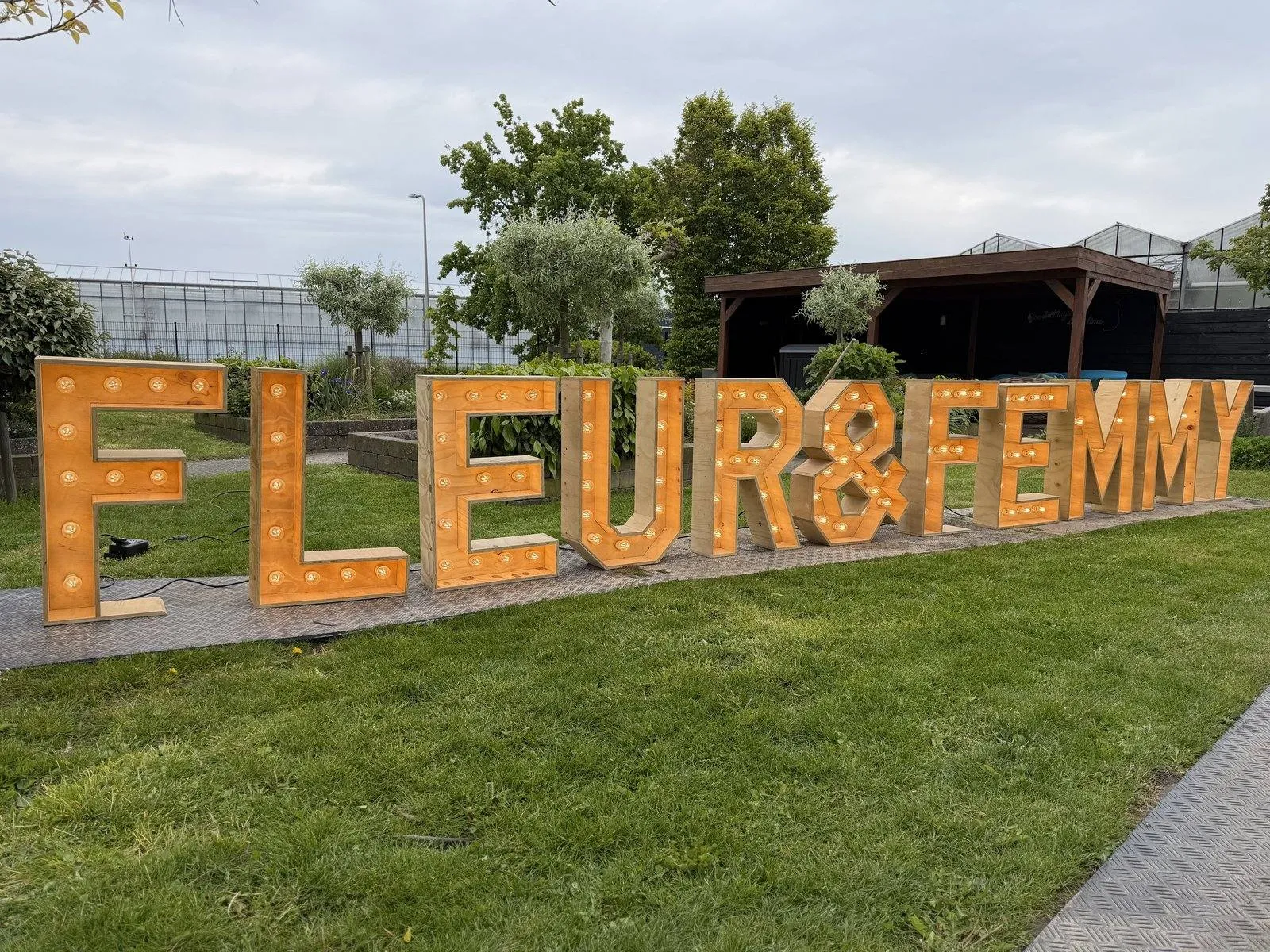 Verlichte houten letters die FLEUR & FEMMY spellen in een tuin
